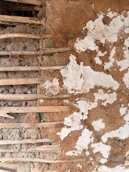 Detailed view of a rustic mud wall with wooden supports, showcasing texture and decay.