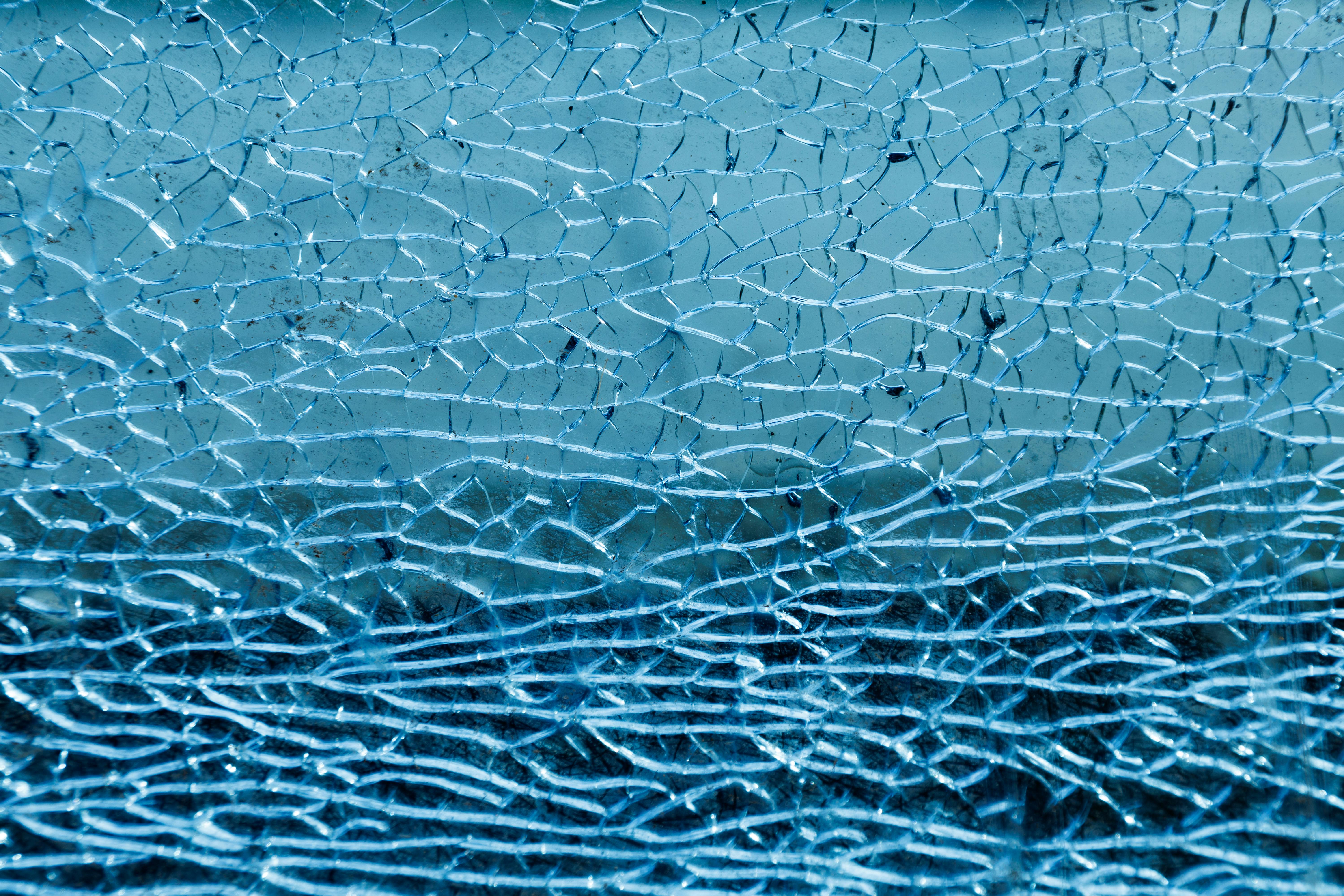 Free Detailed image of cracked glass capturing intricate fractal patterns under blue lighting. Stock Photo