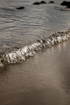 Capturing a tranquil wave gently rippling onto a sandy beach with a soft, reflective surface.