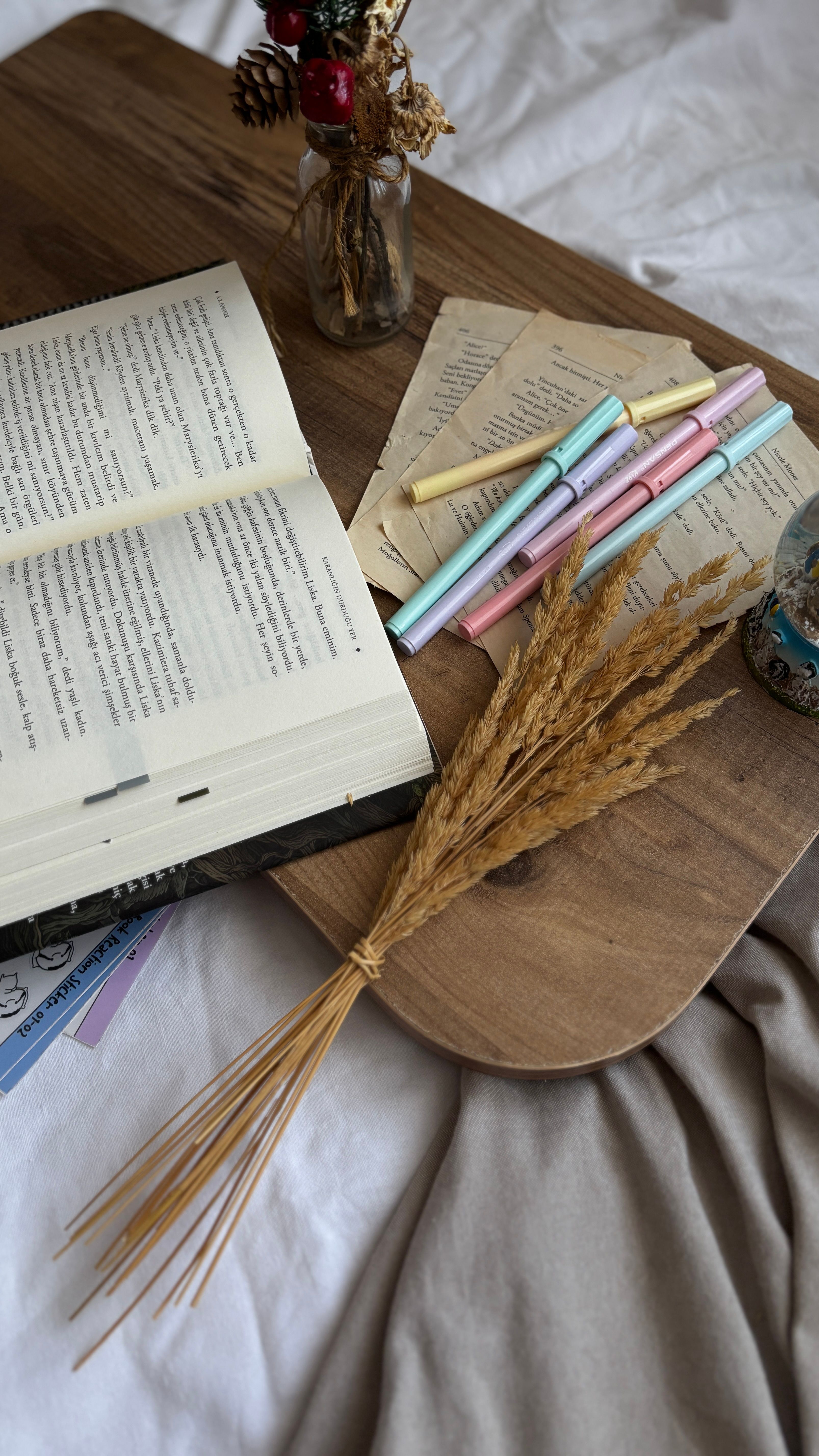 Open book on wooden tray with pastel pens and dried flowers in a cozy setting.