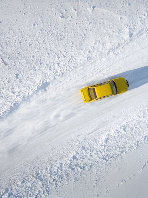 Aerial view of a yellow car drifting on a snow-covered road, showcasing winter adventure and automotive dynamics.