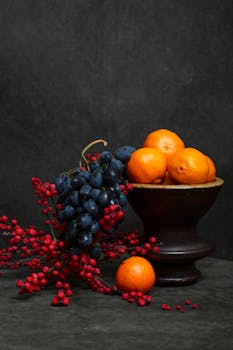 Elegant still life featuring oranges, grapes, and red berries on a dark background.