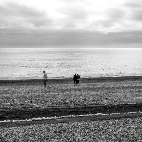 Free Black and white image of people walking on a pebbly beach under cloudy skies. Stock Photo