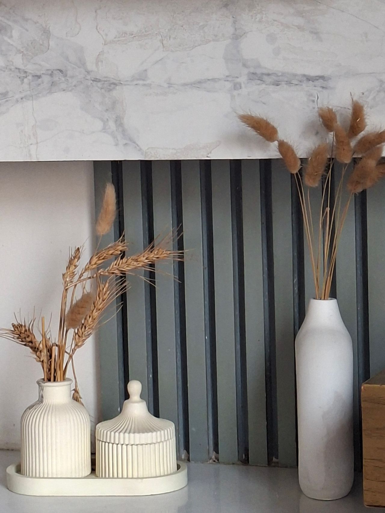 Dried wheat and bunny tail stems in small white vases grouped on a tray
