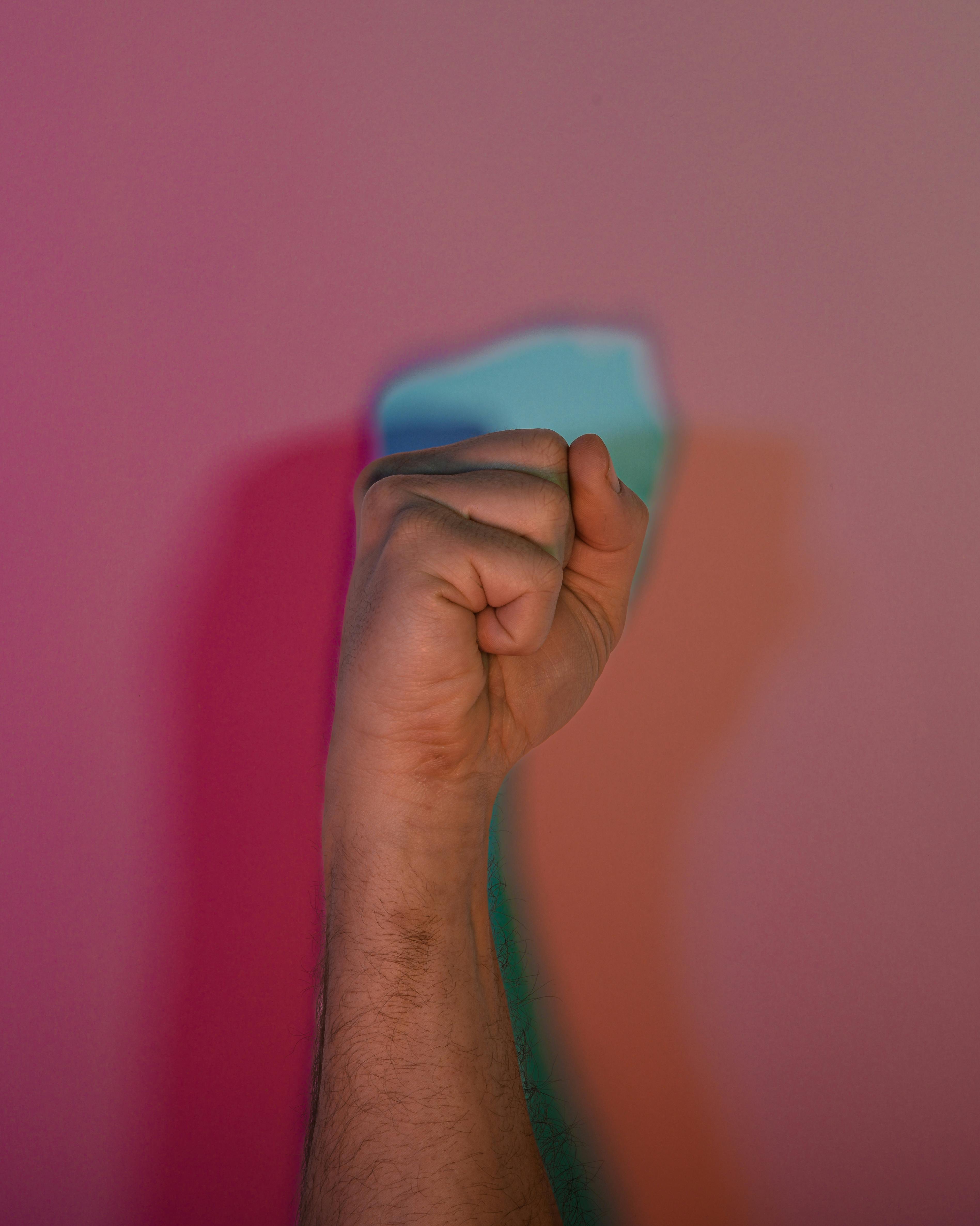 бесплатная Крупный план сжатого кулака на фоне красочной стены, символизирующей силу и единство. Стоковое фото