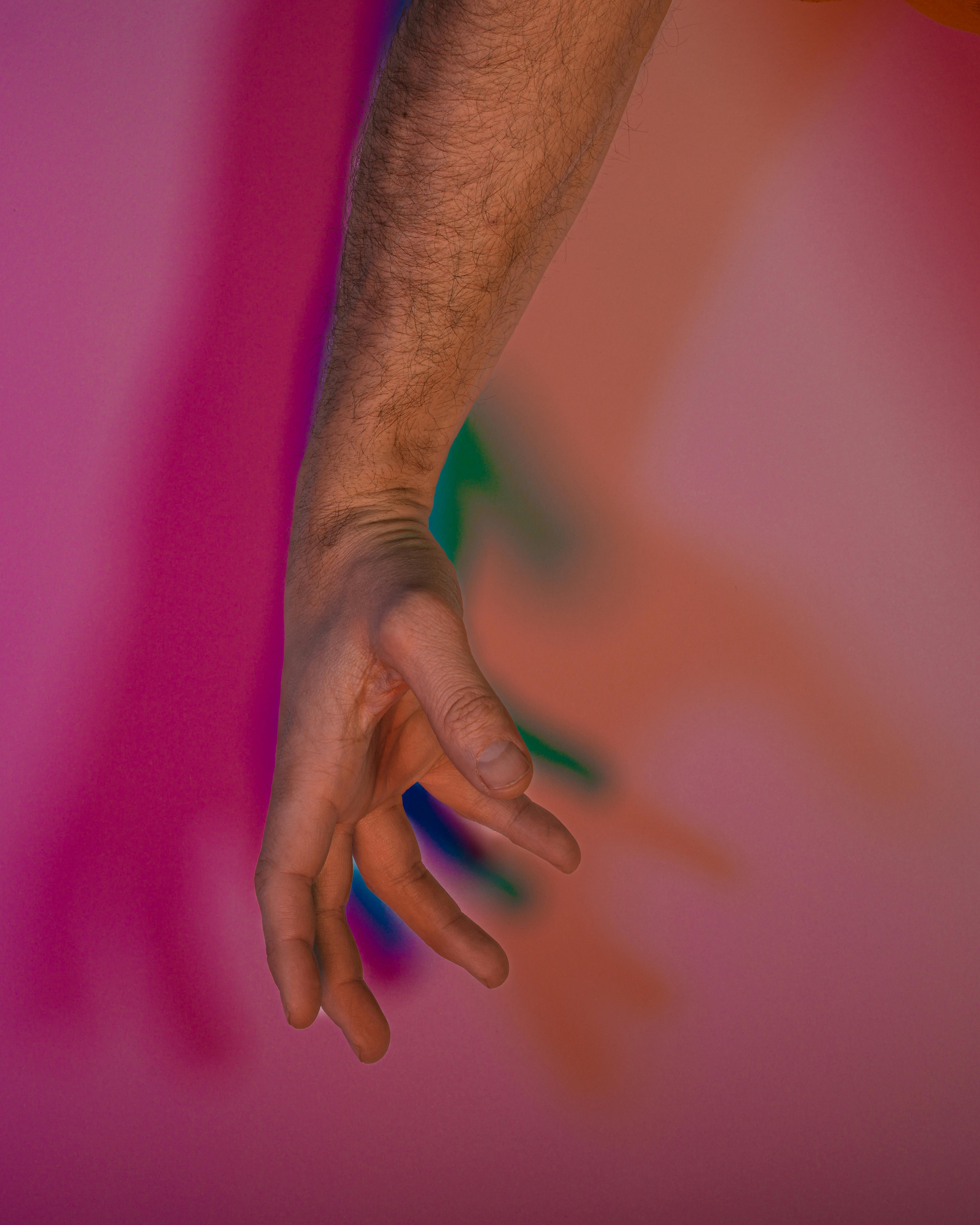 Free An artistic arm with fingers extended casts colorful shadows on a pink gradient background. Stock Photo