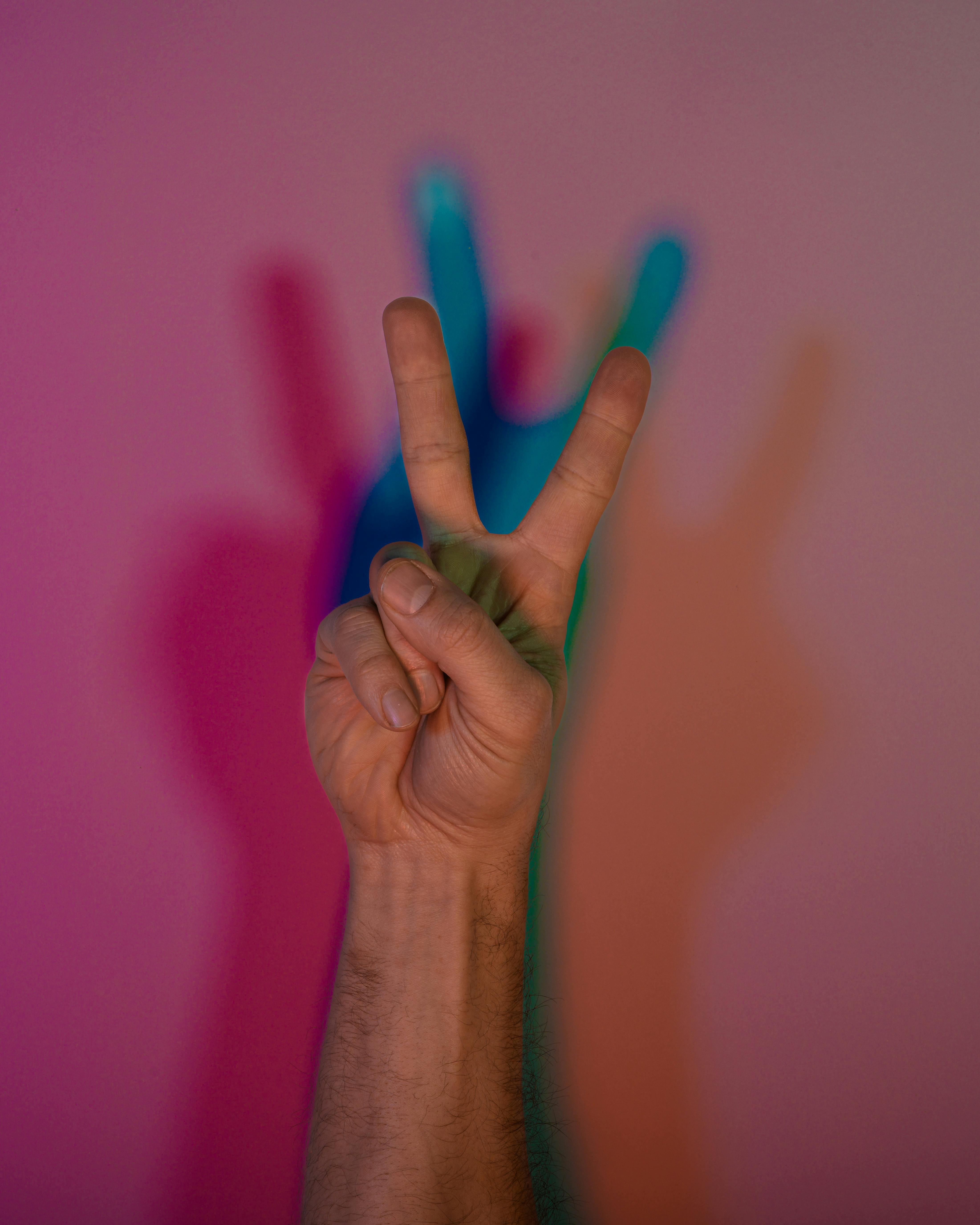 Gratuit Une main faisant le signe de la paix, avec des ombres multicolores éclatantes projetées sur un mur. Photos