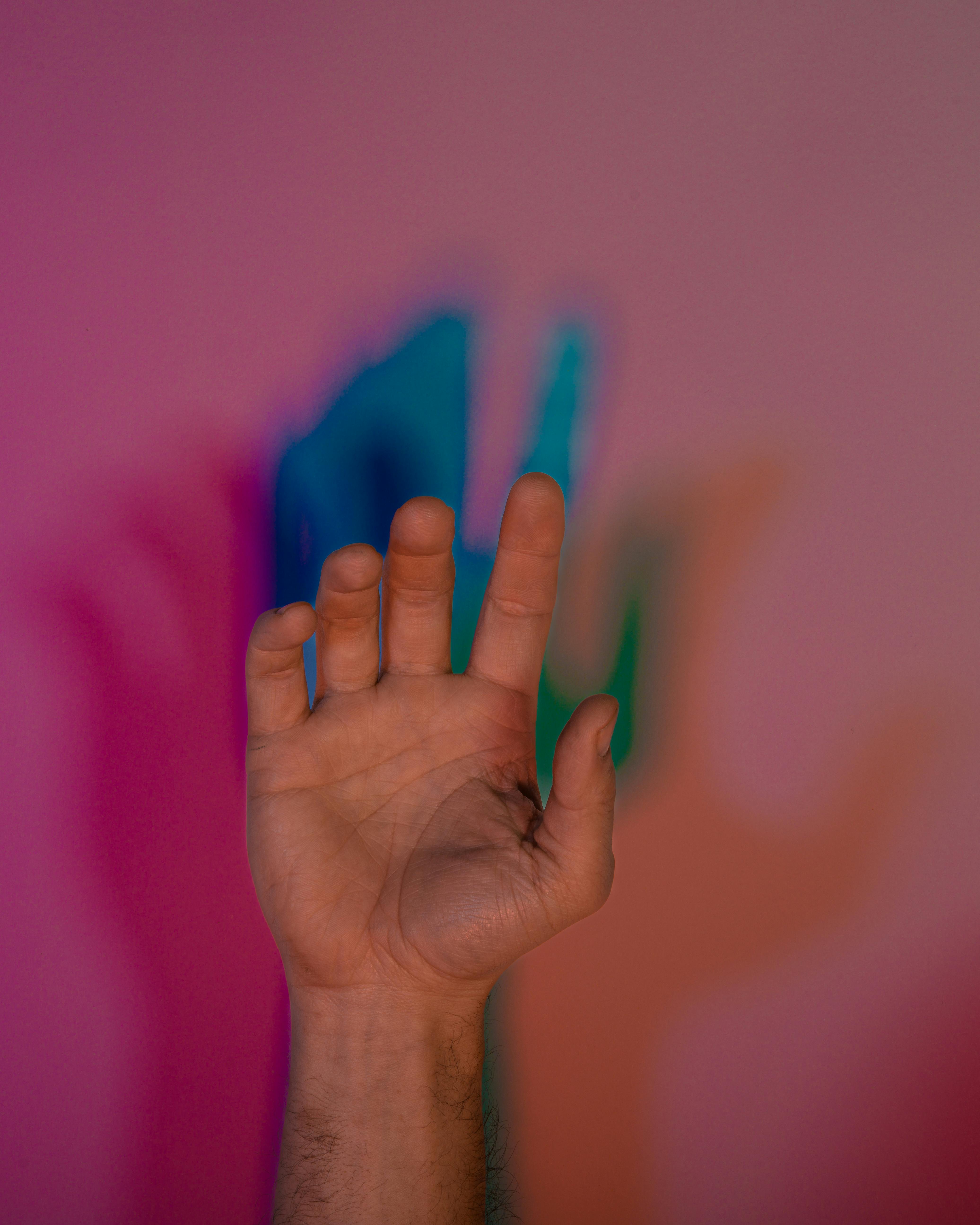 Kostenlos Nahaufnahme einer Hand, die farbenfrohe Schatten auf eine rosa Wand wirft und so einen lebendigen abstrakten Effekt erzeugt. Stock-Foto