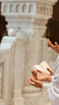 Hands in prayerful gesture near a detailed marble pillar in a place of worship.