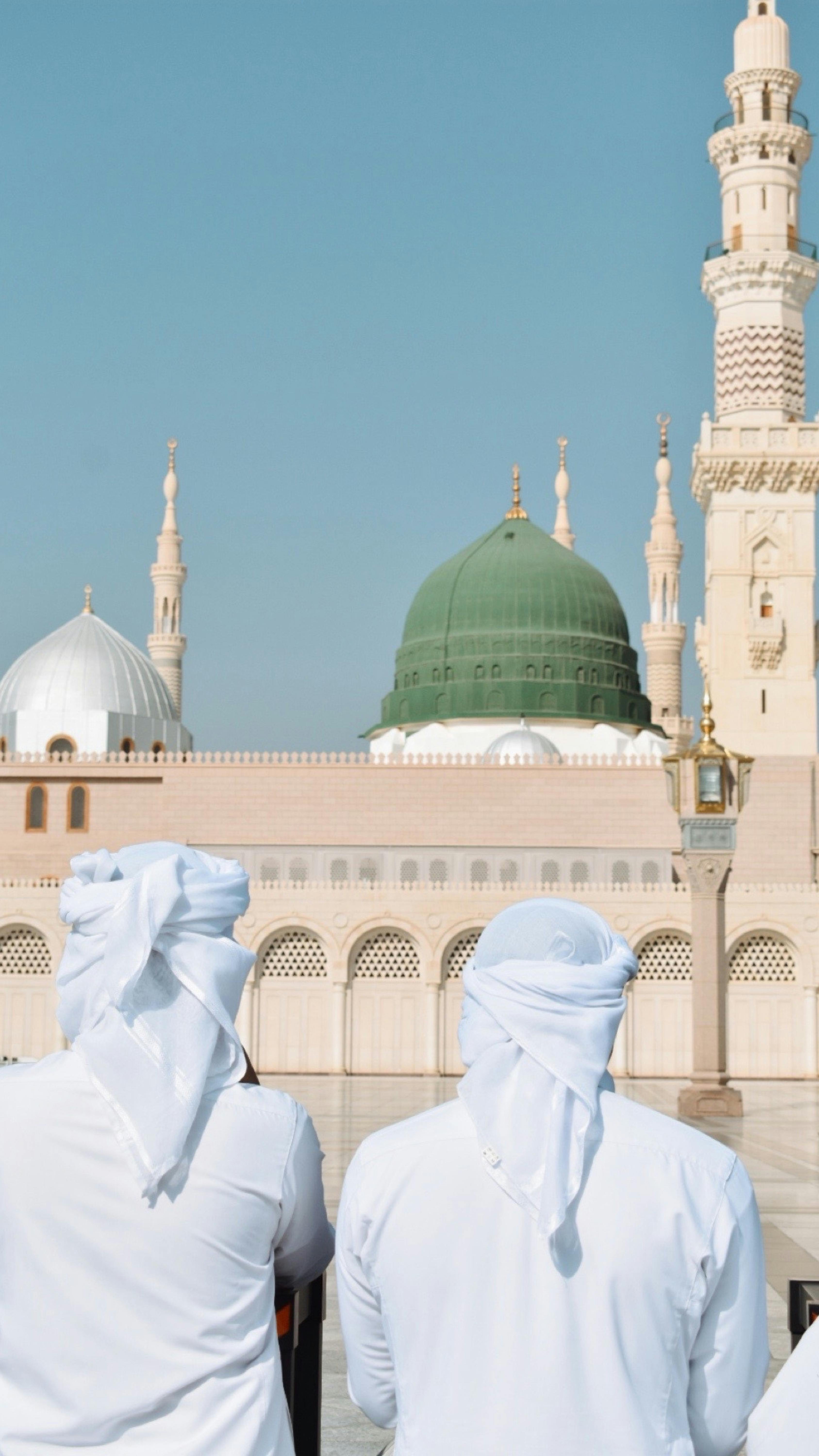 Two men in traditional attire admire Al-Masjid an-Nabawi, a significant Islamic landmark in Medina.