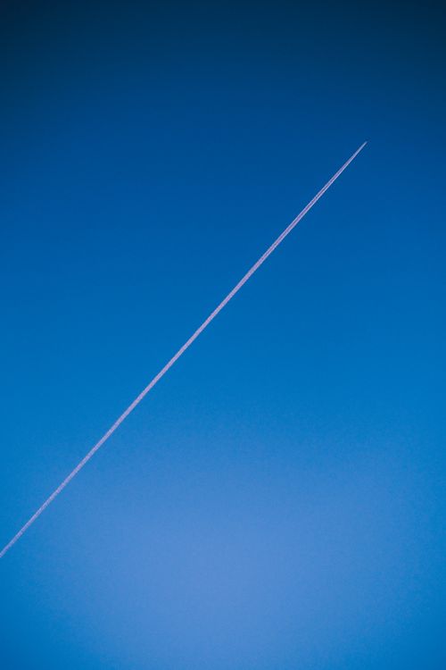 Free A straight contrail stretches across a vibrant blue sky, creating a striking minimalist composition. Stock Photo