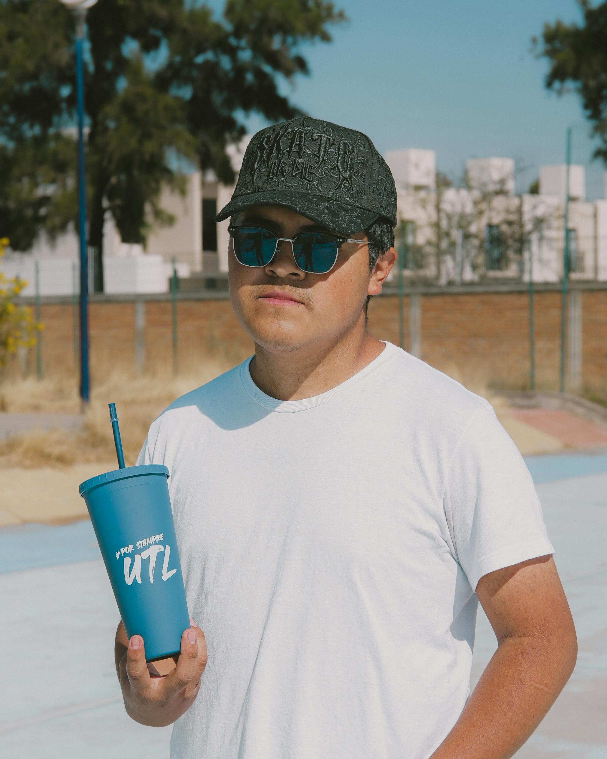 Free A young man in sunglasses and a cap holding a cup, outdoors in León, Mexico. Stock Photo