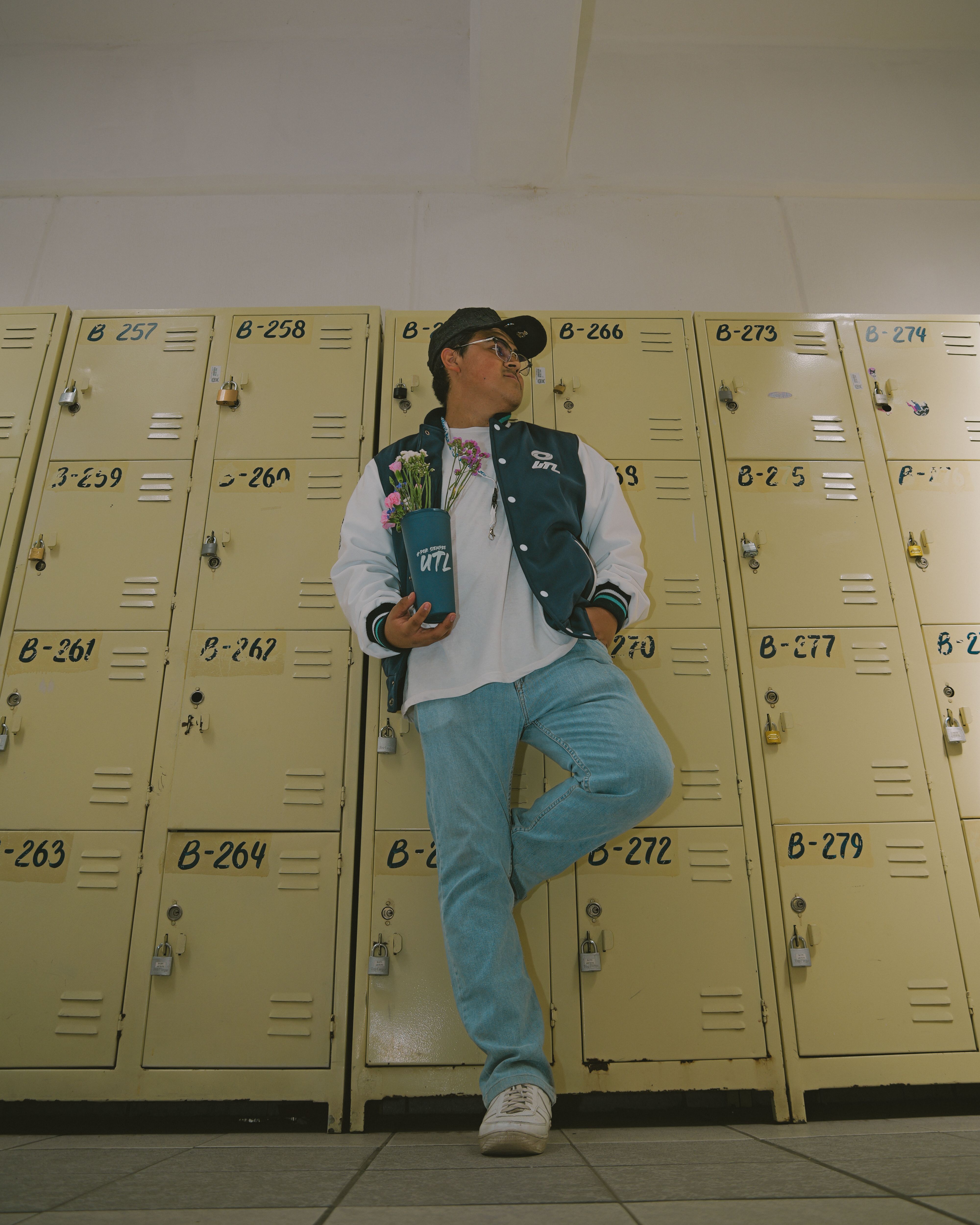 A student leans on lockers with a skateboard in hand at a university hallway.