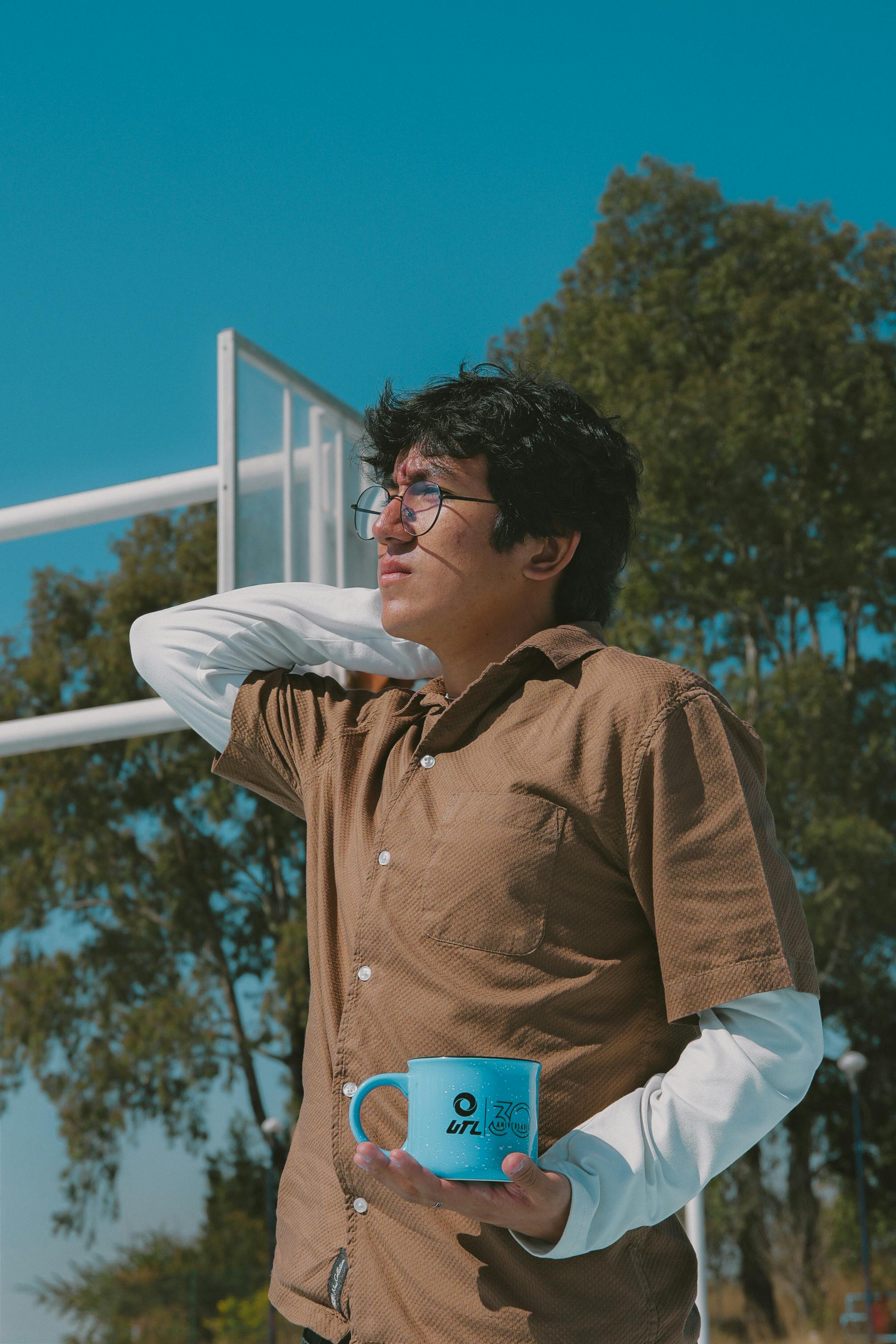 A young man enjoying a sunny day outdoors while holding a blue mug in León, Guanajuato, Mexico.