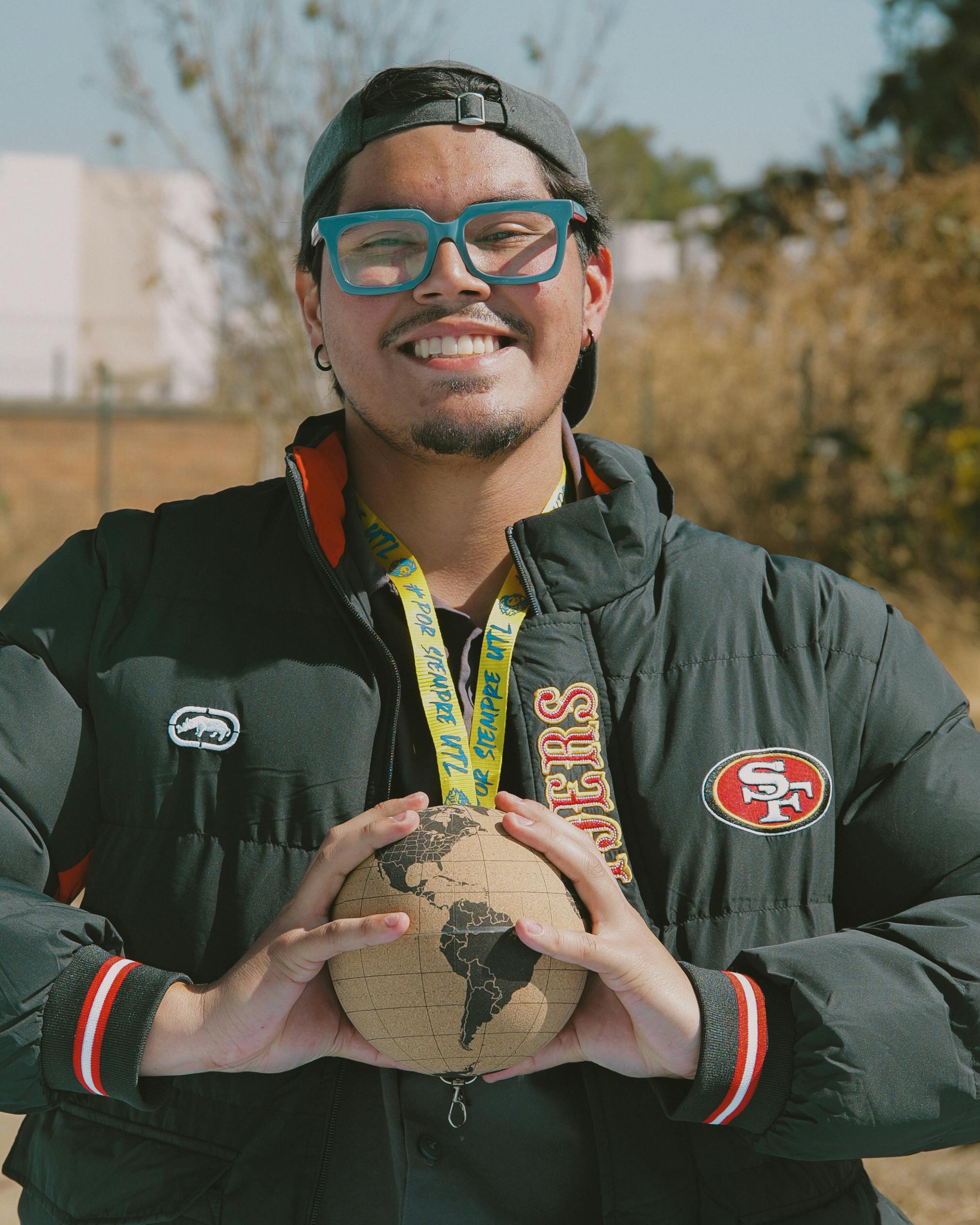 Cheerful man with glasses holding a globe outdoors on a sunny day.