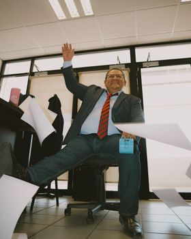 Cheerful businessman in office throws papers to celebrate success, exuding happiness.
