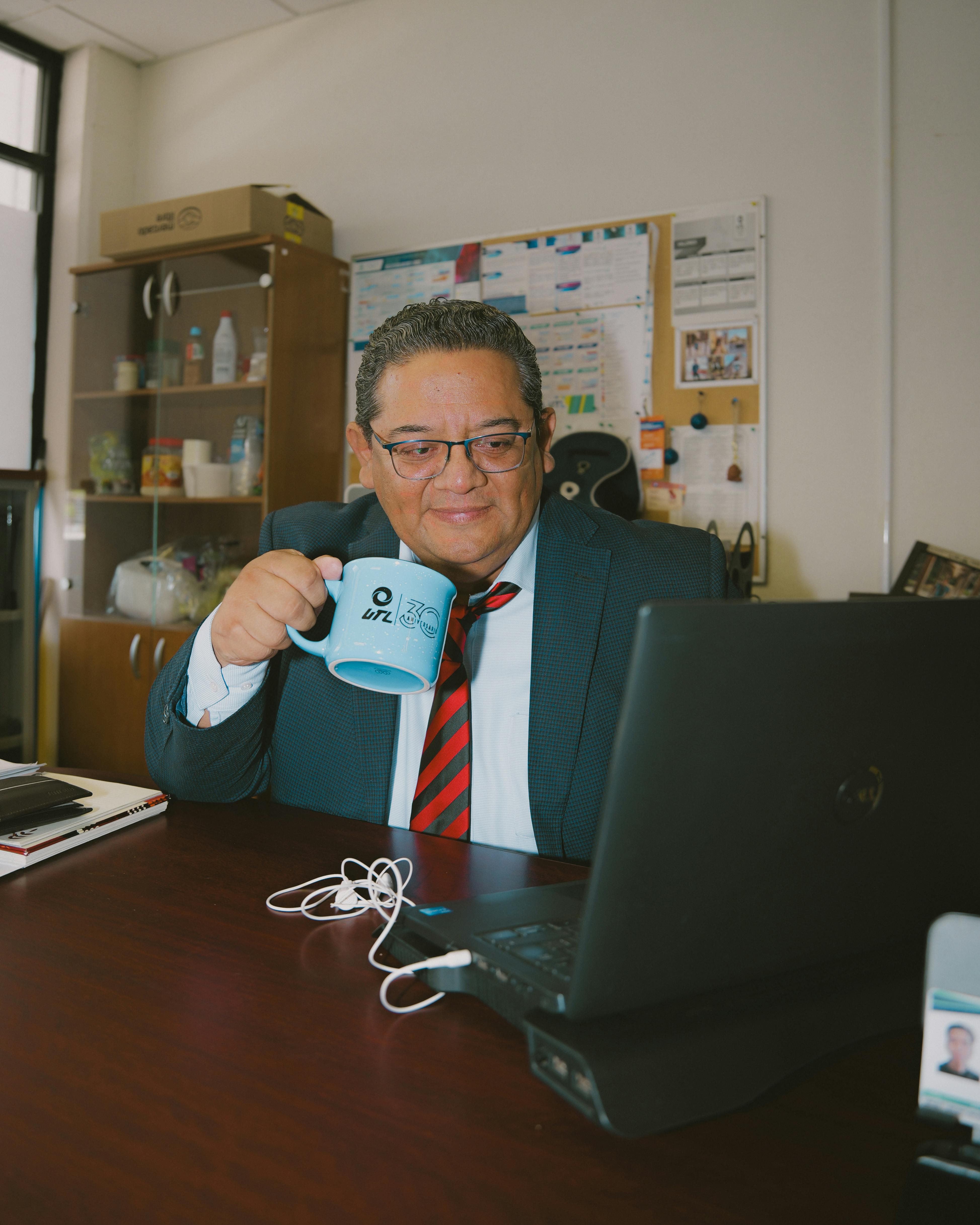 Professional adult man working at office, sipping coffee, focused on laptop.