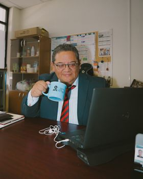 Professional adult man working at office, sipping coffee, focused on laptop.