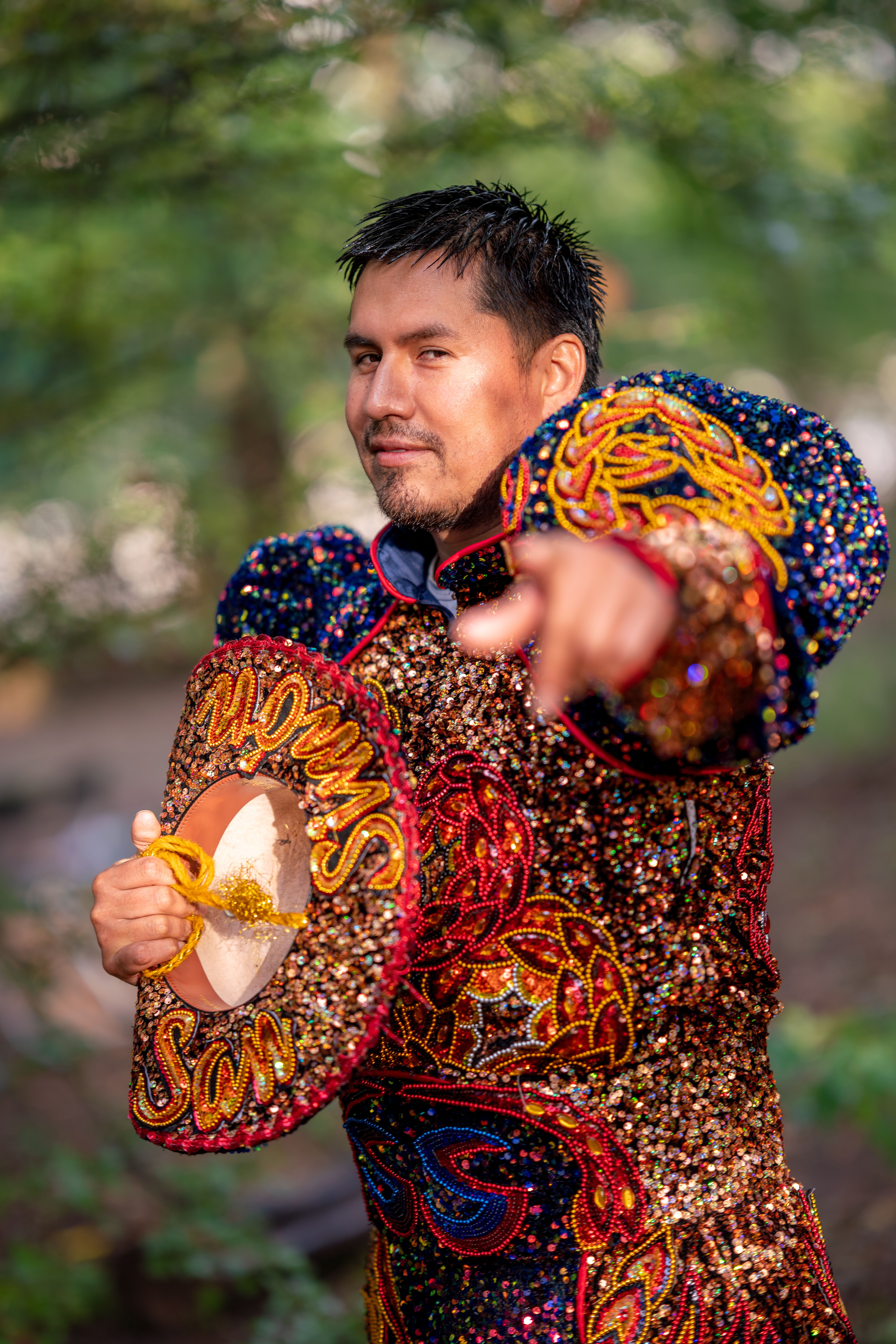 A man in a vibrant traditional costume poses outdoors, showcasing colorful embroidery.