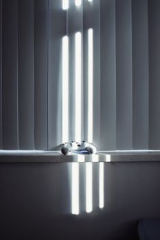 A video game controller bathed in sunlight shining through blinds, creating dramatic shadows inside a room.