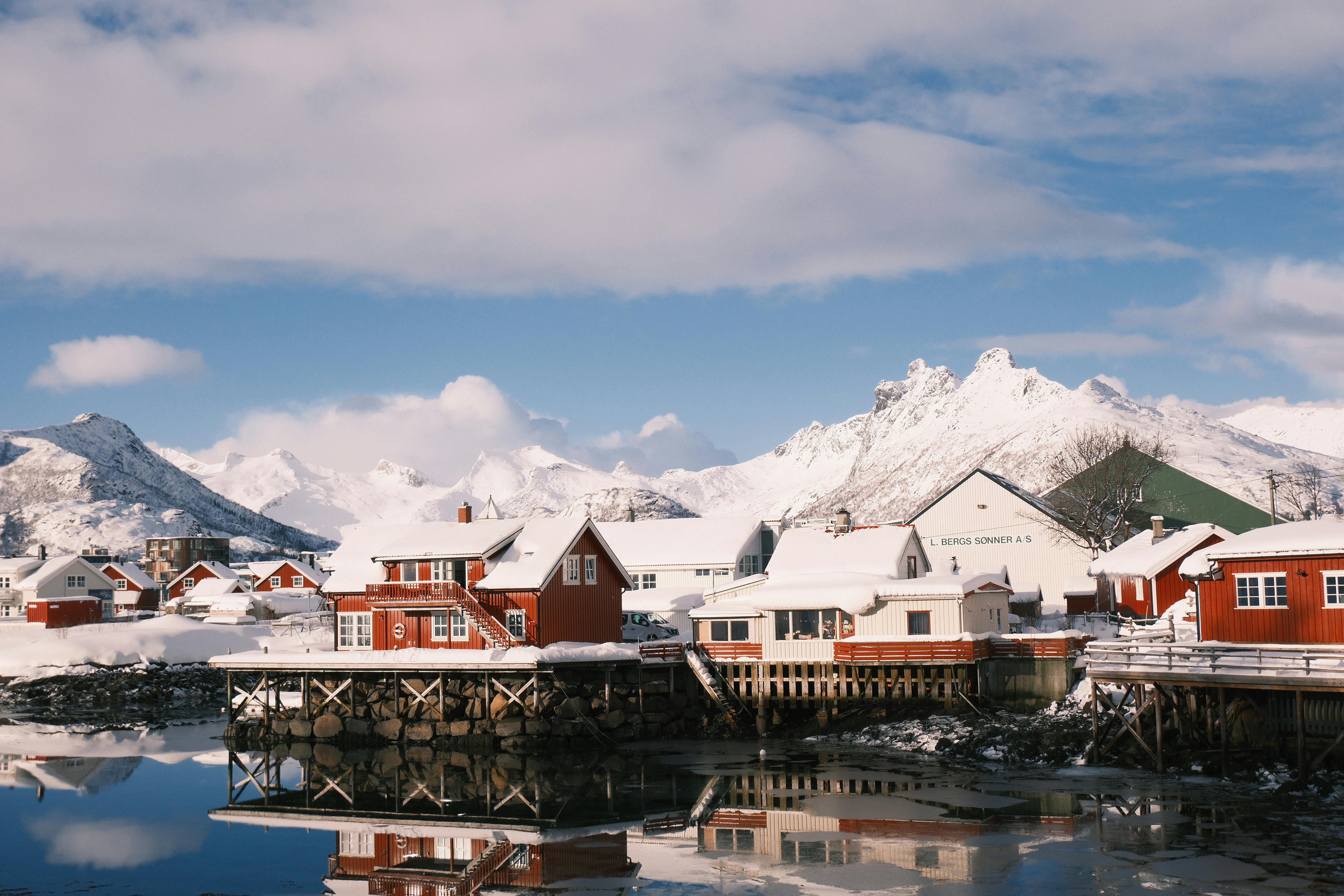 Captivating winter view of the snow-covered coastal town of Svolvær in Norway, featuring traditional red houses and a mountain backdrop.