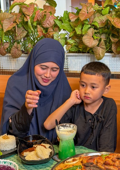 Free A mother and child share a meal in a restaurant surrounded by lush plants. Stock Photo