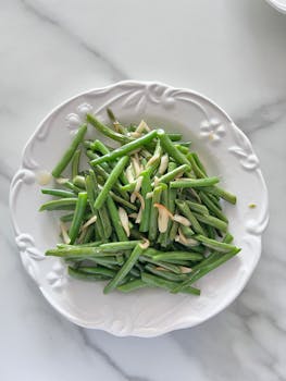A delicious fresh green bean salad garnished with sliced almonds on a white plate.