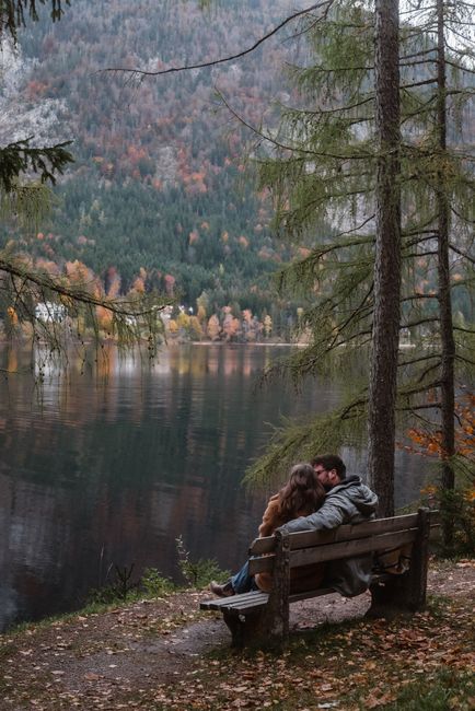 Couple embraces on a lakeside bench in a serene autumn setting.