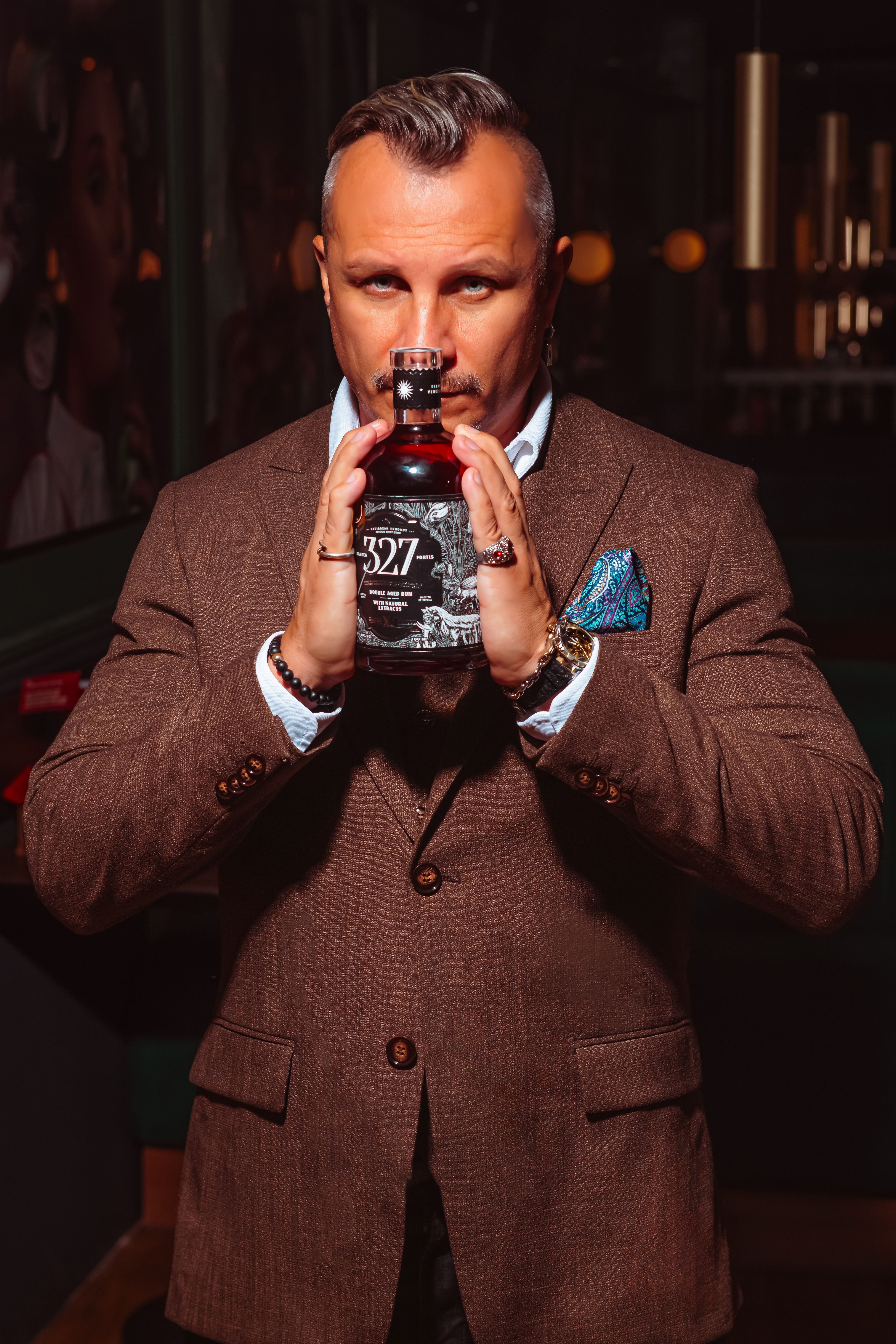 A sophisticated man in a brown suit holding a vintage whiskey bottle, exuding charisma and elegance.