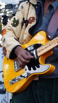 Close-up of a musician playing a bright yellow electric guitar outdoors, showcasing artistic style and vibrant energy.