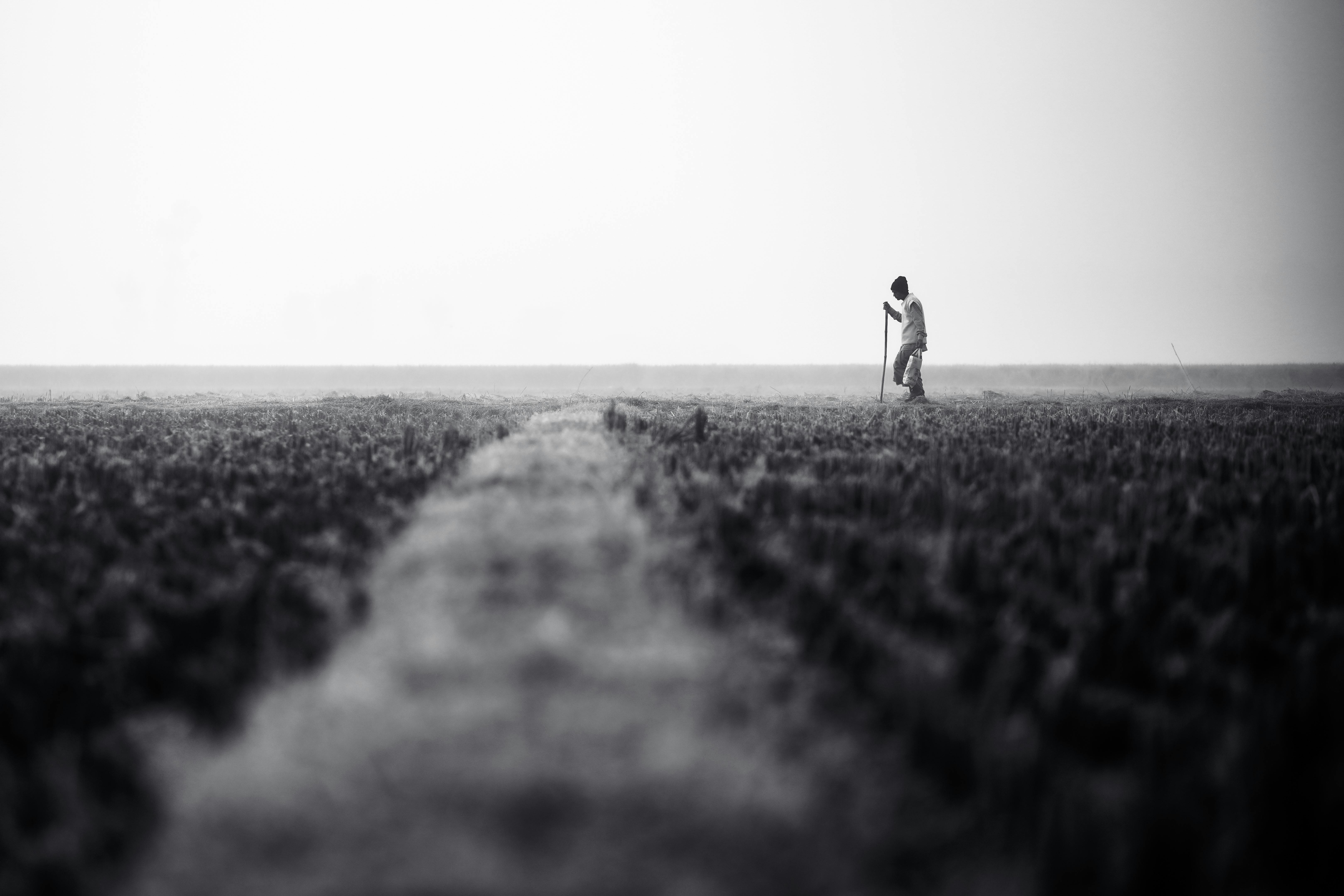 Free A solitary figure traverses a wide, barren field in a contemplative black and white scene. Stock Photo