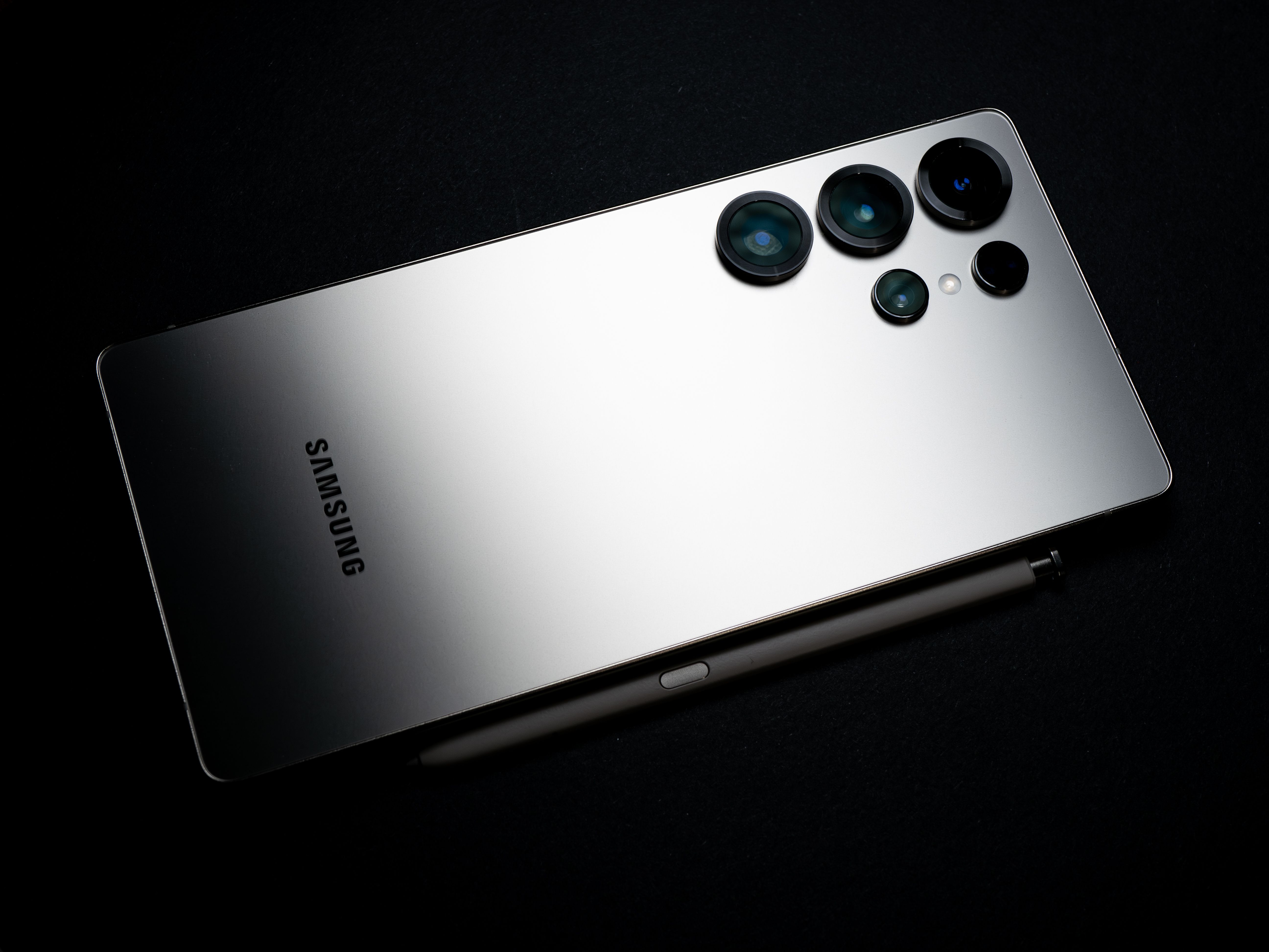 Back view of a silver smartphone with camera lenses and a stylus, set against a dark backdrop.