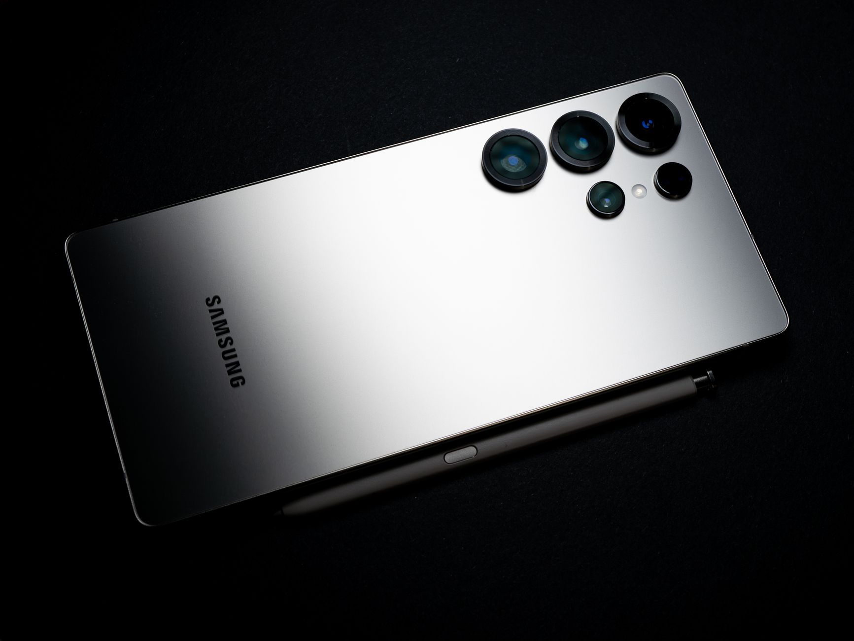 Back view of a silver smartphone with camera lenses and a stylus, set against a dark backdrop.
