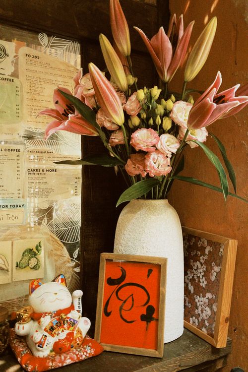 Free A beautiful floral arrangement with lilies and carnations beside a traditional lucky cat figurine. Stock Photo