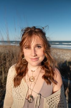 Smiling young woman with red hair and glasses at a beach on a sunny day. Natural and carefree vibe.