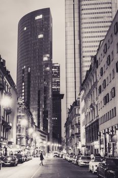 Sepia-toned view of a bustling Frankfurt street with modern skyscrapers at night.