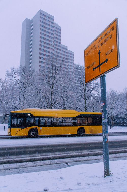 Free Yellow bus on a snowy street near a high-rise in Berlin, Germany, with a directional sign. Stock Photo