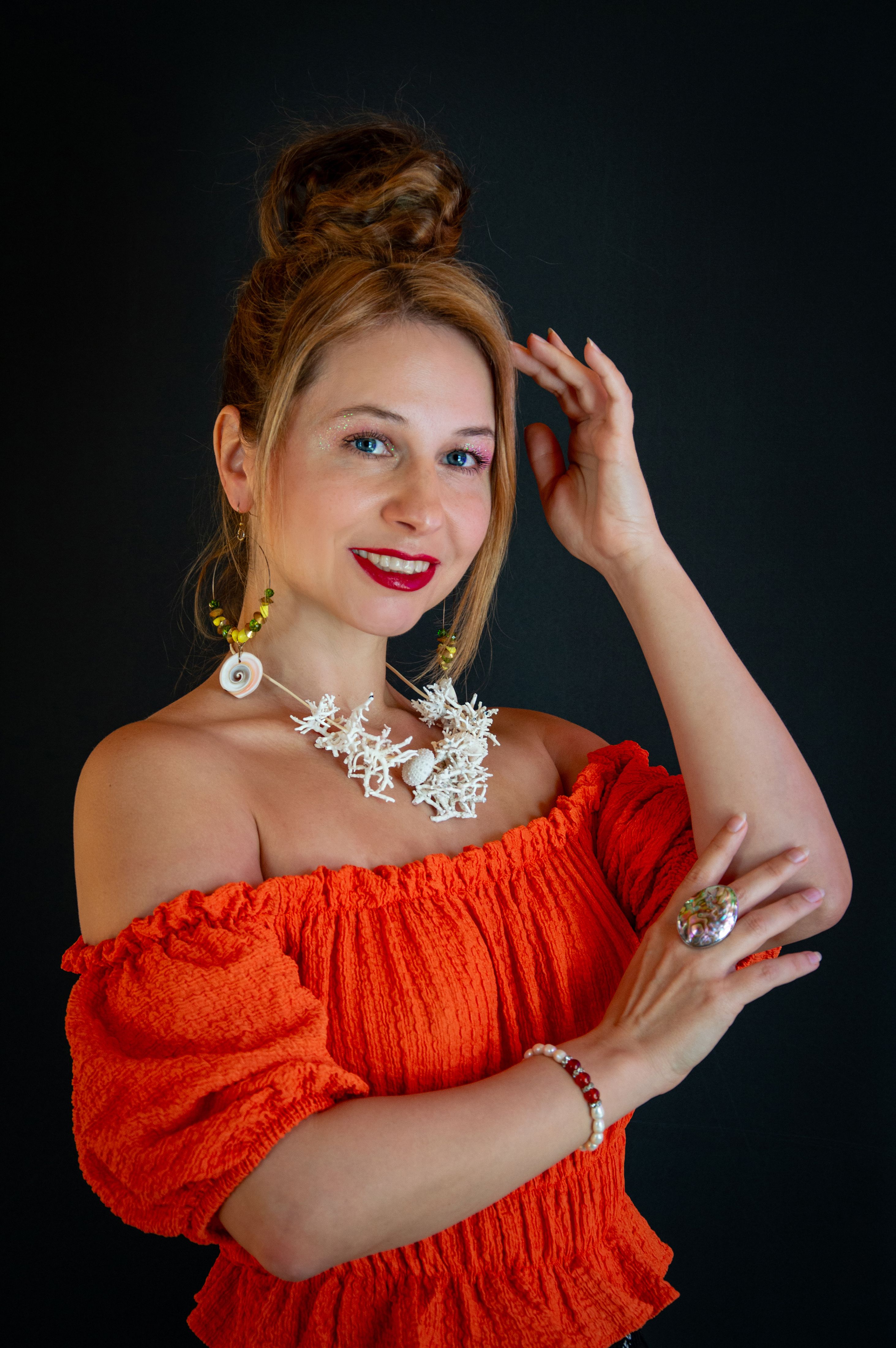 Stylish woman in orange dress with elegant jewelry against a dark background.