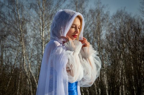 Free A woman in a white hooded cloak stands gracefully in a serene winter forest. Stock Photo