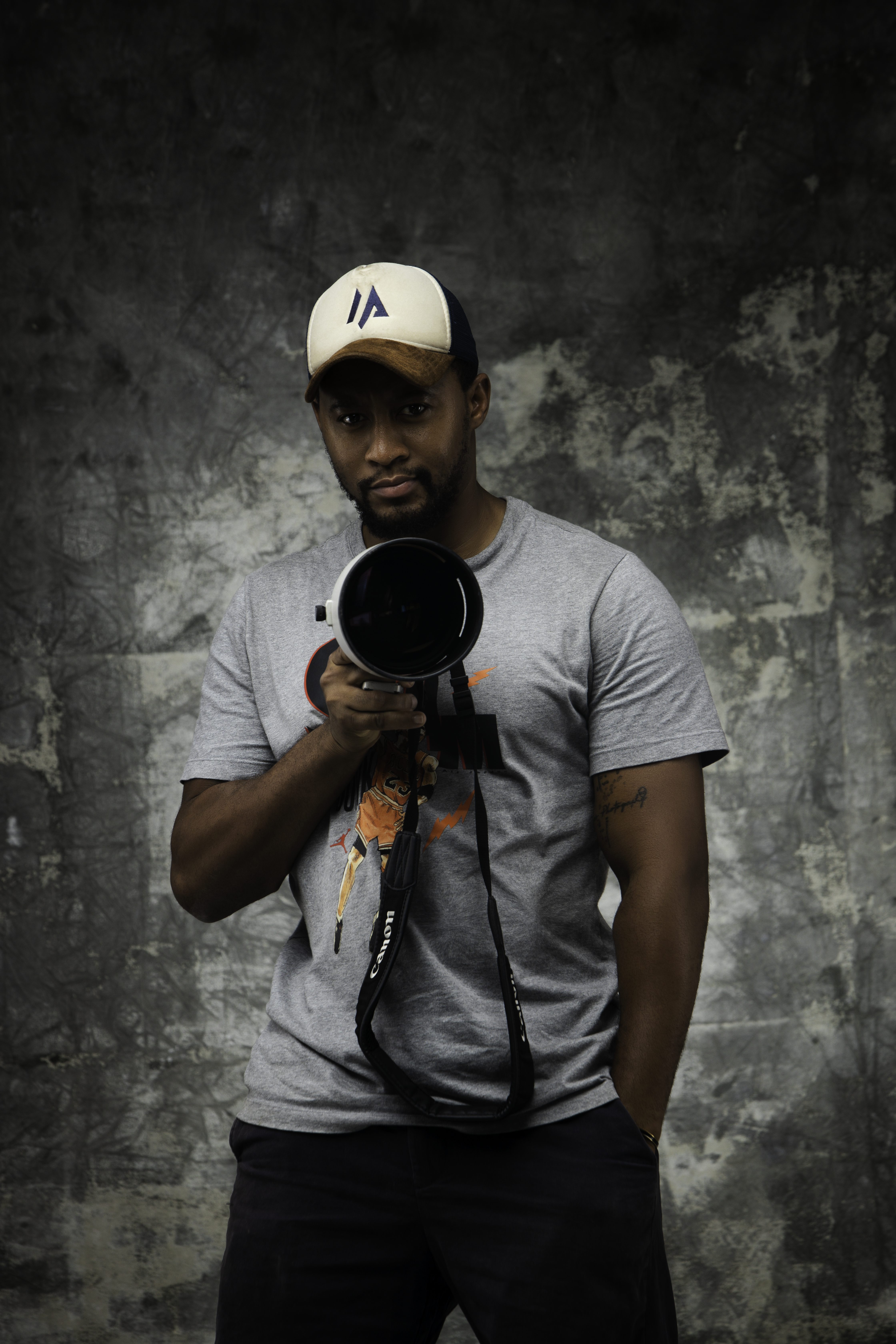 Serious photographer posing with a camera lens against a textured backdrop.
