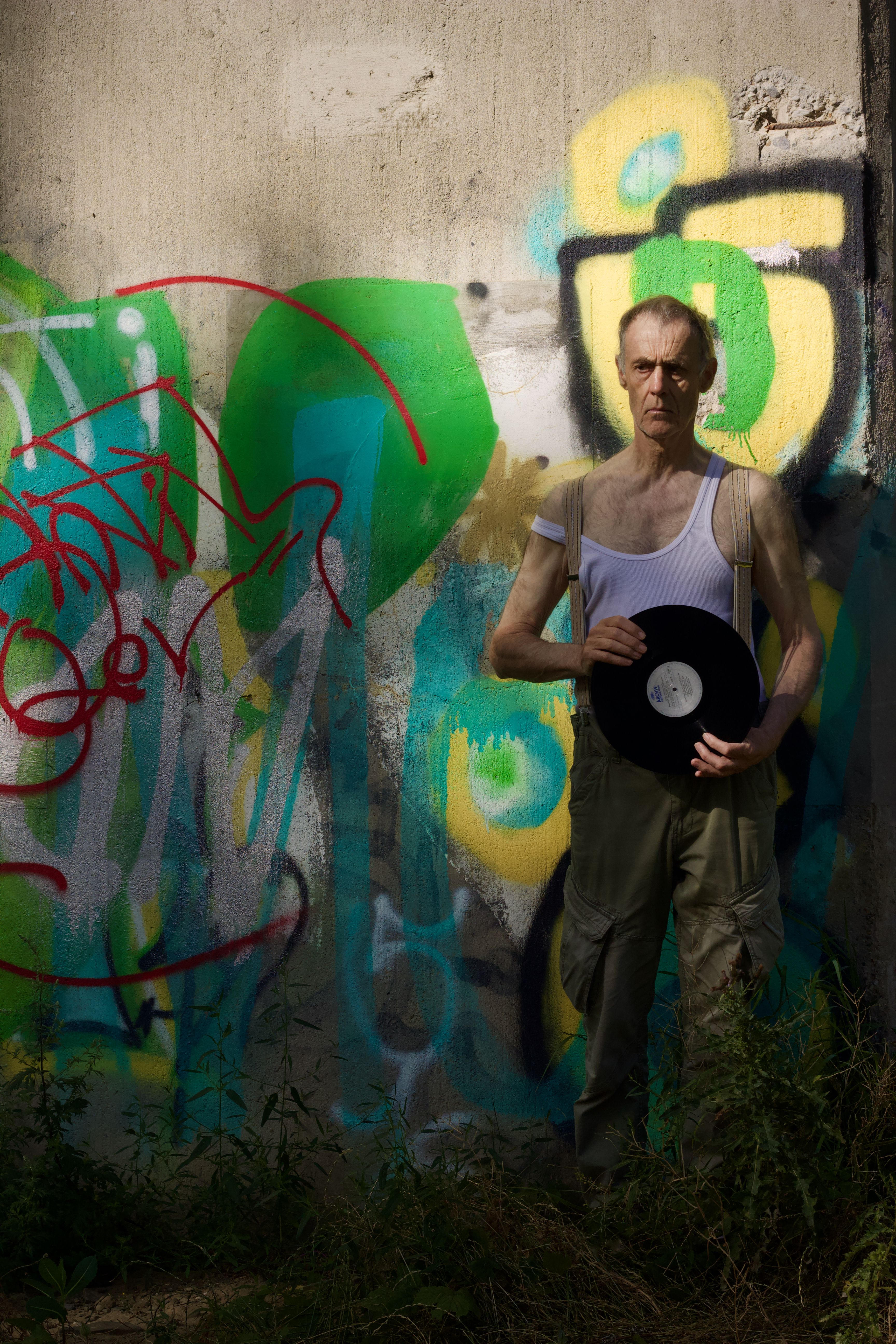 Man standing in front of graffiti wall holding a vinyl record, urban mood.