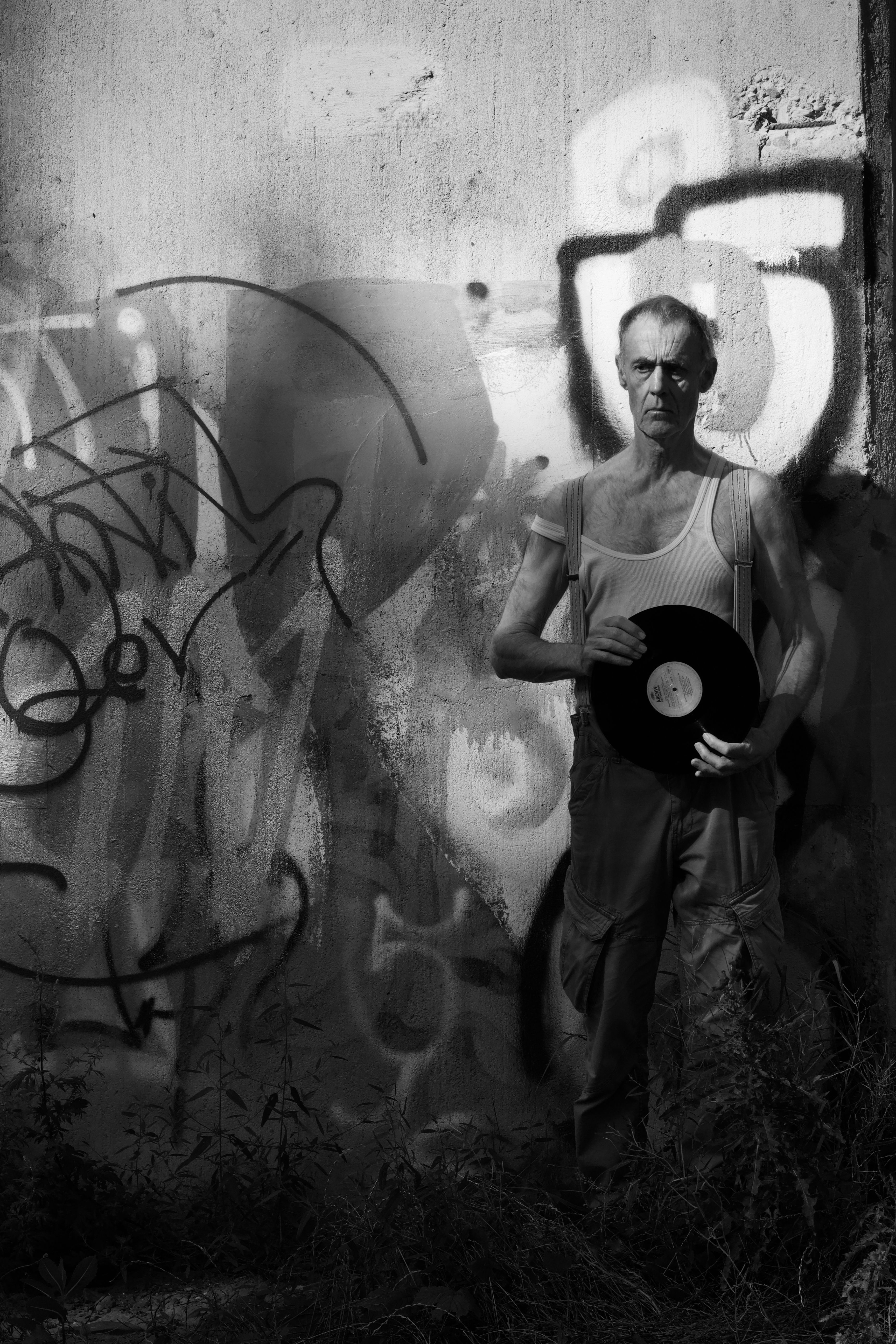 Artistic portrait of a man holding a vinyl record against a graffiti wall.