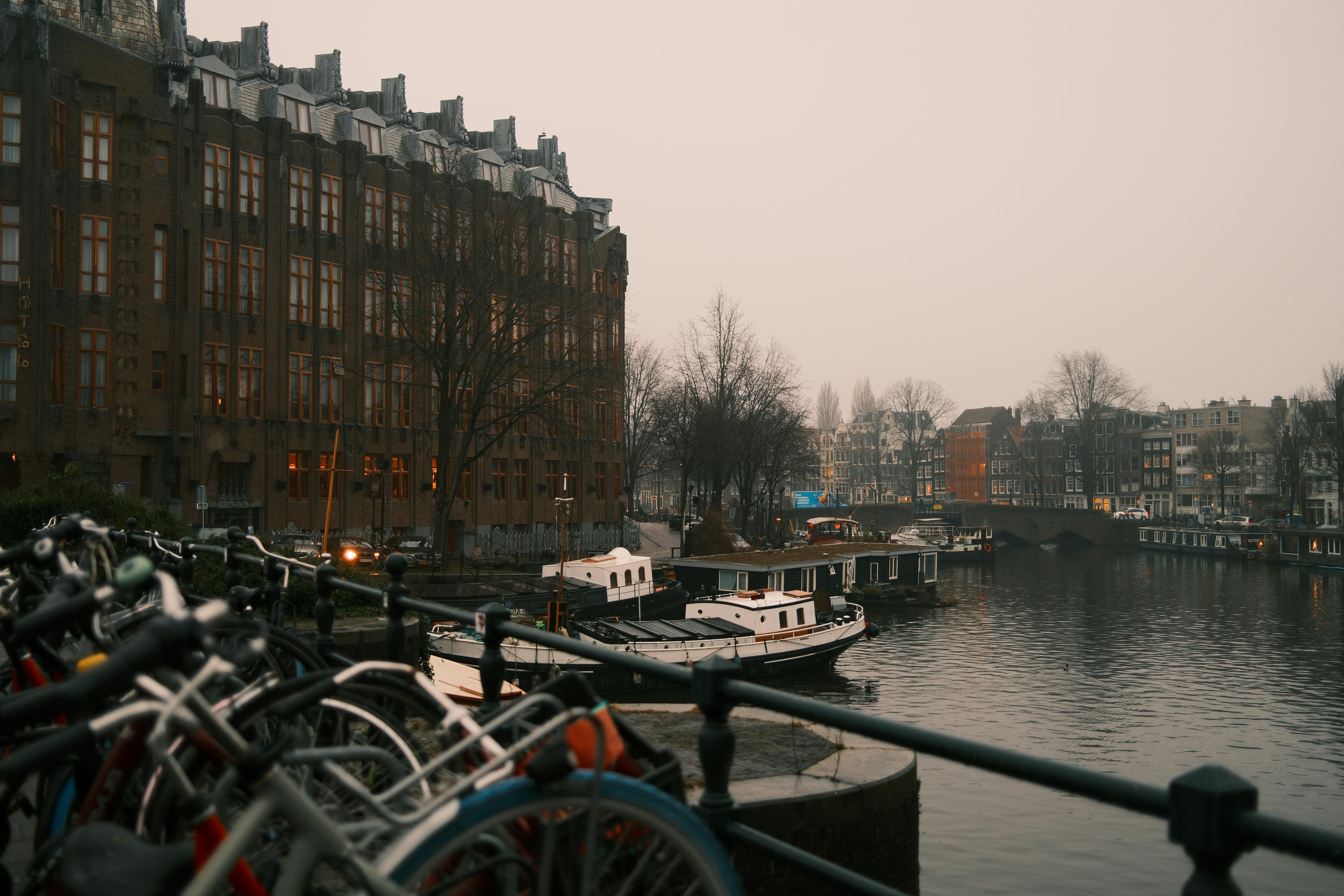 бесплатная Живописный вечерний вид на амстердамский канал, лодки и велосипеды на фоне классической архитектуры. Стоковое фото