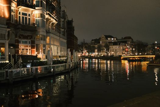 Scenic night view of Amsterdam canal with illuminated buildings reflected on water.