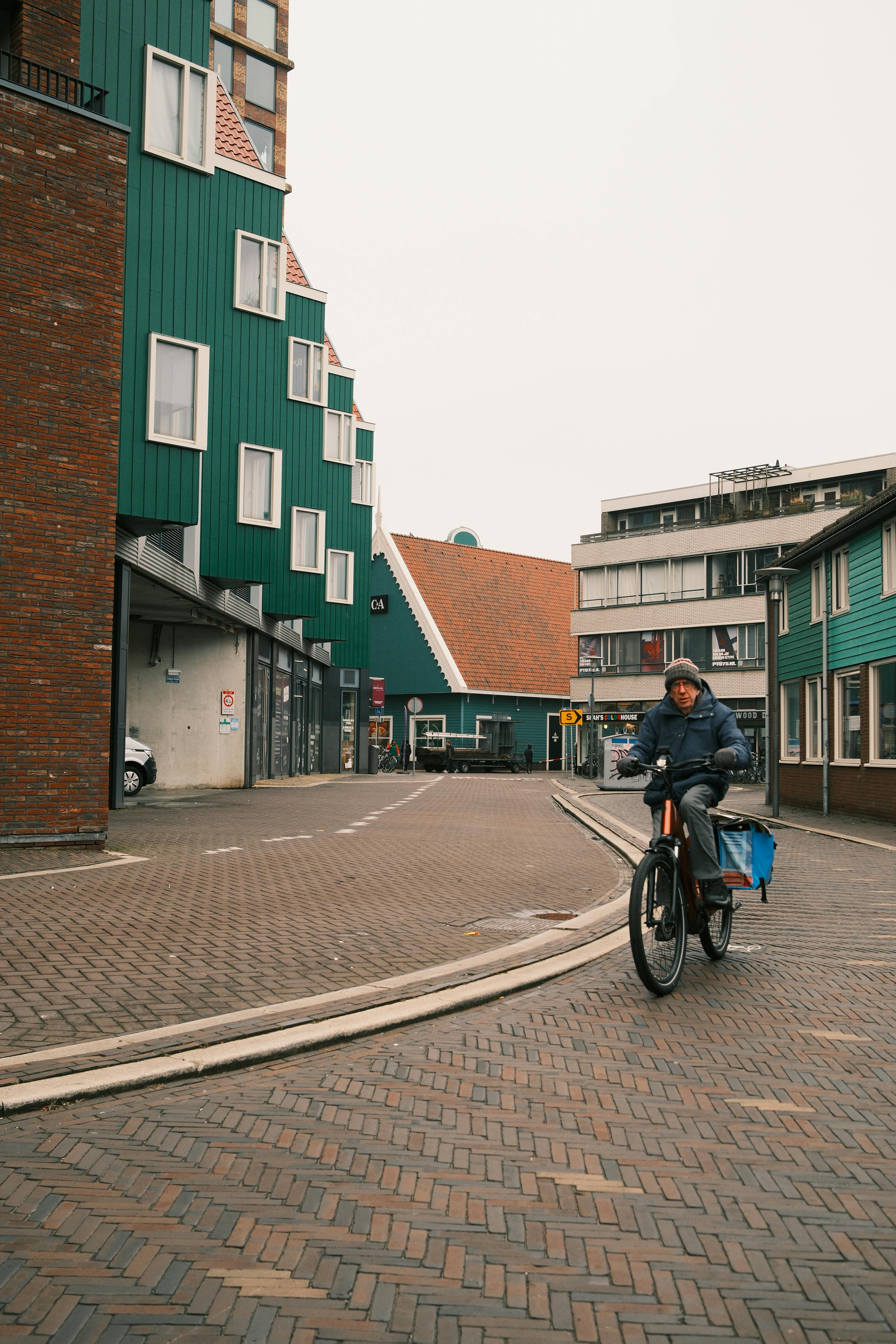 бесплатная Велосипедист проезжает мимо характерных зеленых зданий в очаровательном европейском квартале. Стоковое фото