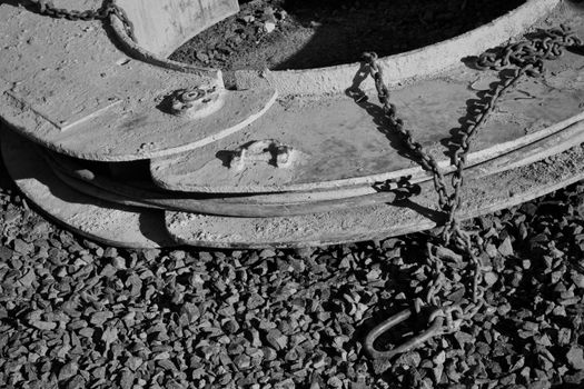 Detailed black and white image of industrial chains and metal parts on pebbled ground.