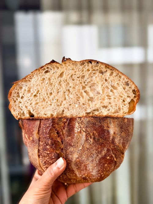 Free Hand holding freshly baked artisan sourdough with a rustic crust, showcasing the texture of the bread Stock Photo
