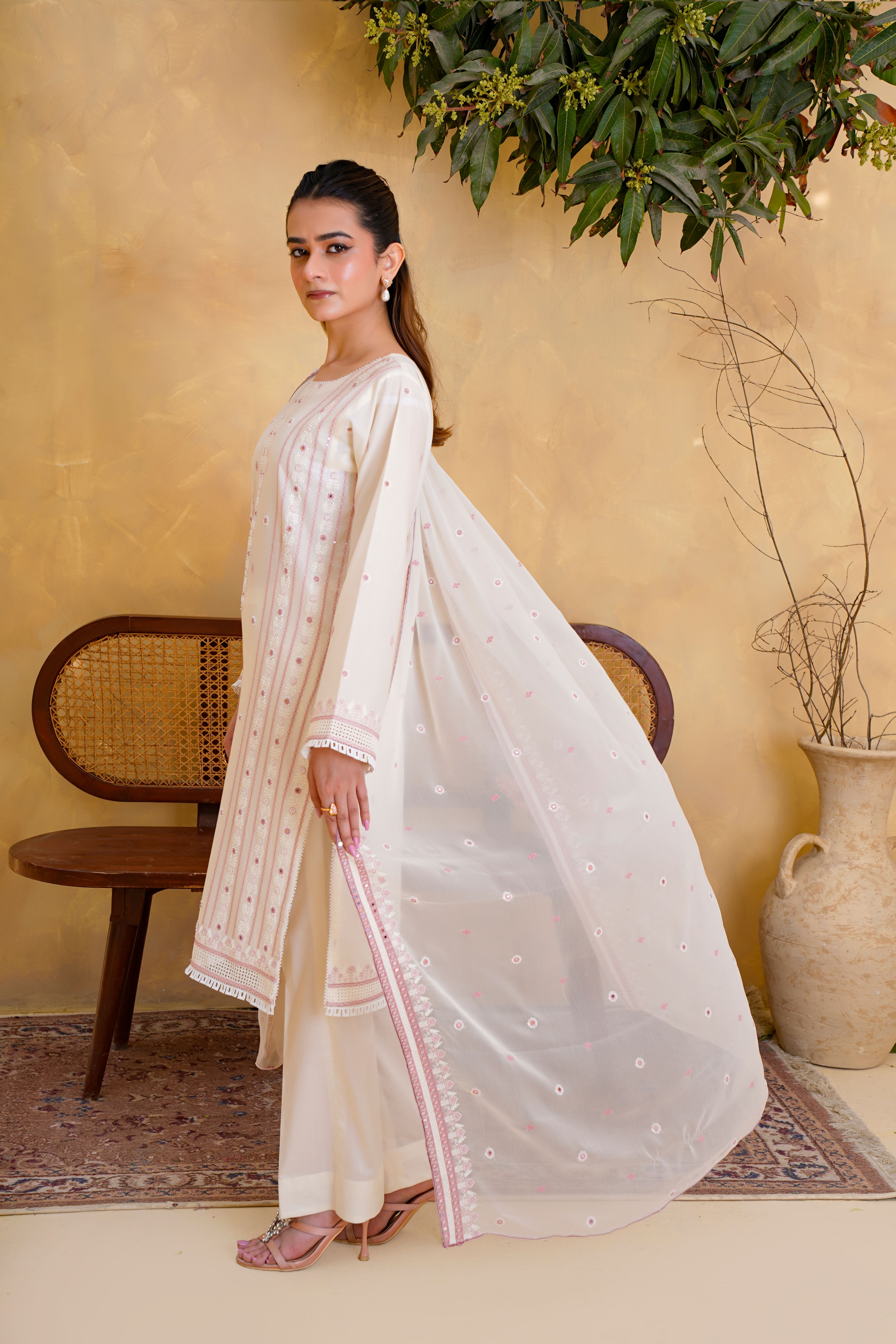 Woman modeling traditional embroidered dress with sheer dupatta indoors.
