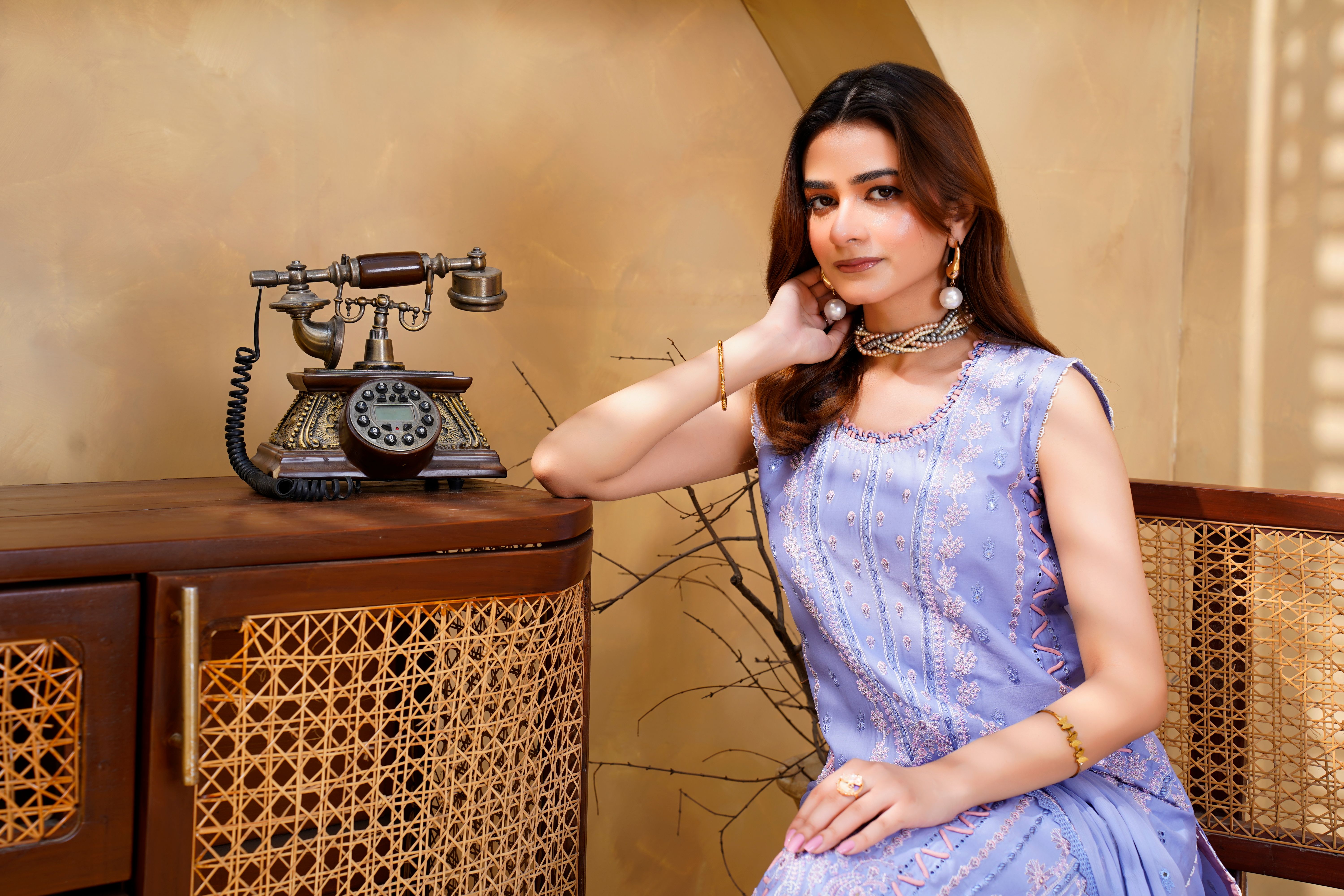 Young woman in embroidered dress posing indoors with vintage telephone in Lahore.