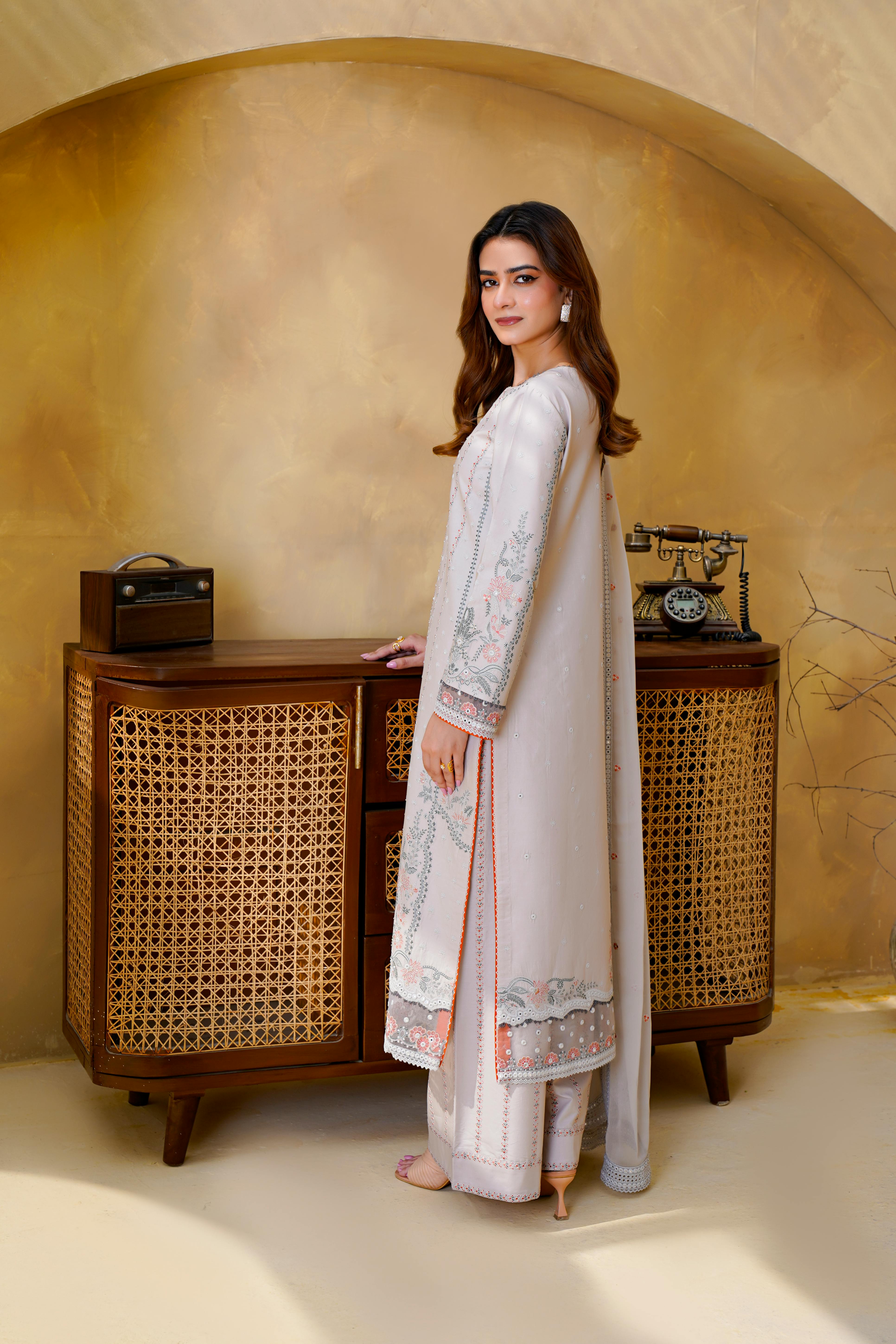 Woman in embroidered eastern dress standing by a vintage cabinet.